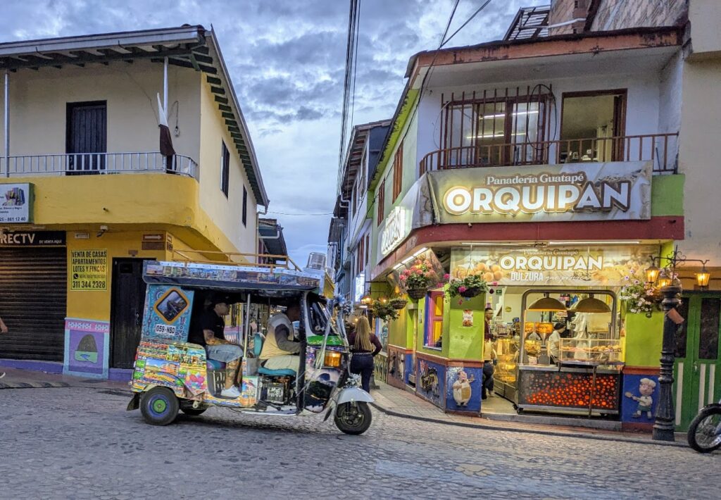 Colorful tuk-tuk parked on a cobblestone street in front of a bakery in Colombia during dusk